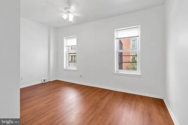 an empty room with wooden floor chandelier fan and windows