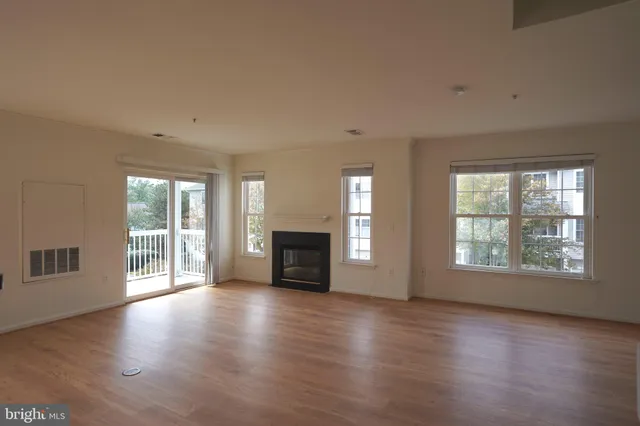 an empty room with wooden floor fireplace and windows