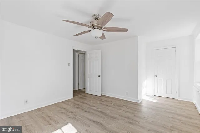 a view of an empty room with wooden floor and a ceiling fan