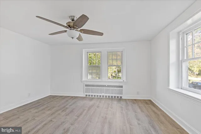 an empty room with wooden floor windows and fan