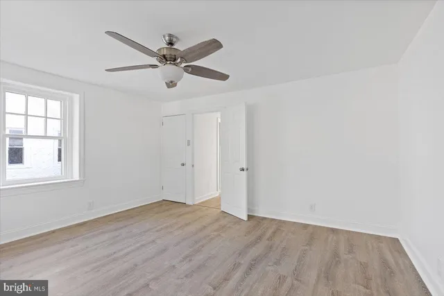 an empty room with wooden floor a ceiling fan and windows