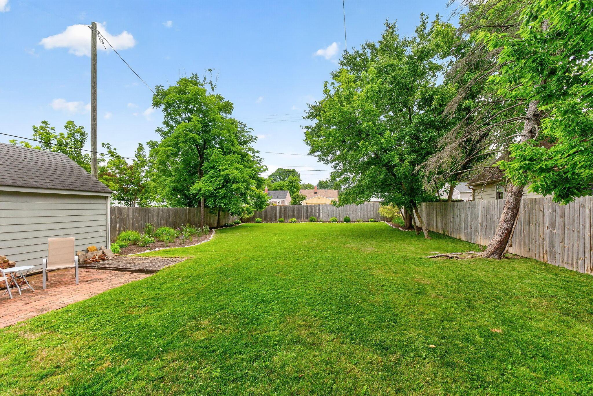 492 Wetmore Road Columbus, OH 43214 - Photo 44 of 55 Expansive backyard featuring a lush lawn, mature trees, wood fence, and a brick paver patio
