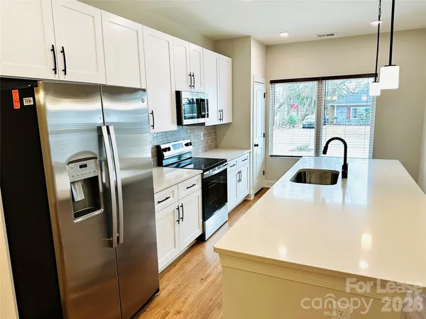 a kitchen with stainless steel appliances granite countertop a refrigerator a sink a stove and white cabinets with wooden floor