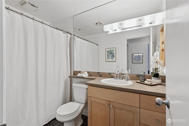 a bathroom with a granite countertop sink a toilet a mirror and shower curtain