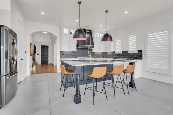 a kitchen with stainless steel appliances granite countertop a kitchen island a stove a refrigerator a sink a dining table and chairs with wooden floor