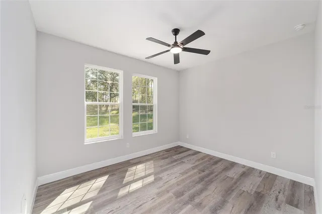 an empty room with wooden floor fan and windows