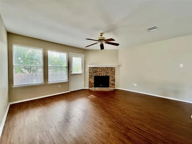 an empty room with wooden floor fireplace and windows