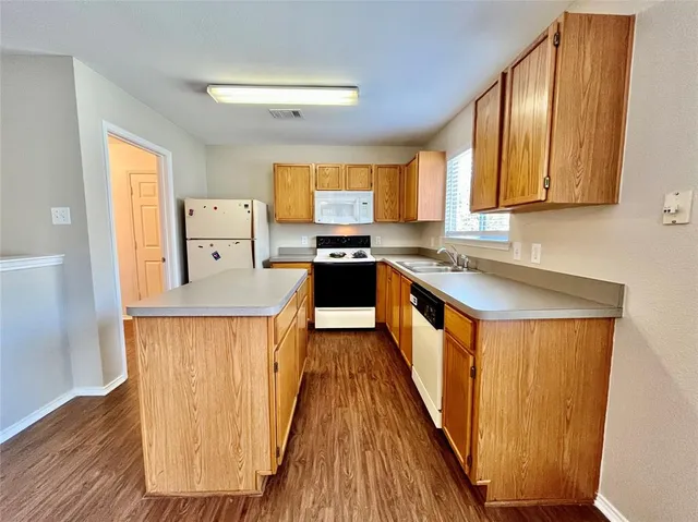 a kitchen with stainless steel appliances granite countertop wooden cabinets a sink a stove a refrigerator and dishwasher with wooden floor