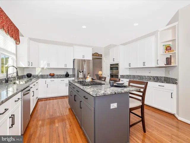 a kitchen with stainless steel appliances granite countertop a stove top oven a sink dishwasher and a refrigerator with wooden floor