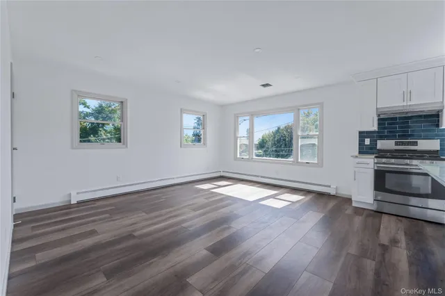 an empty room with wooden floor windows and kitchen view