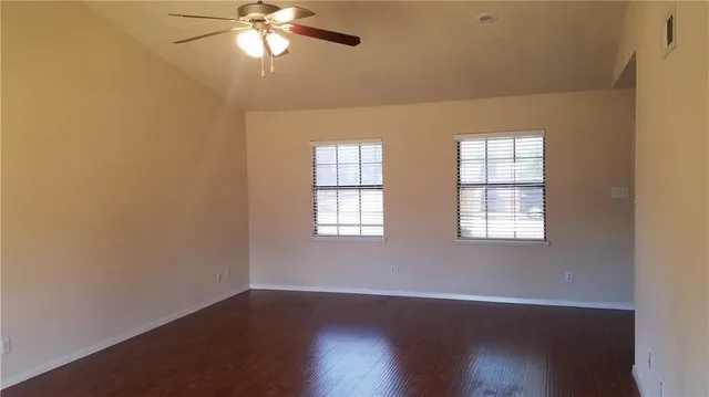 an empty room with wooden floor chandelier fan and windows