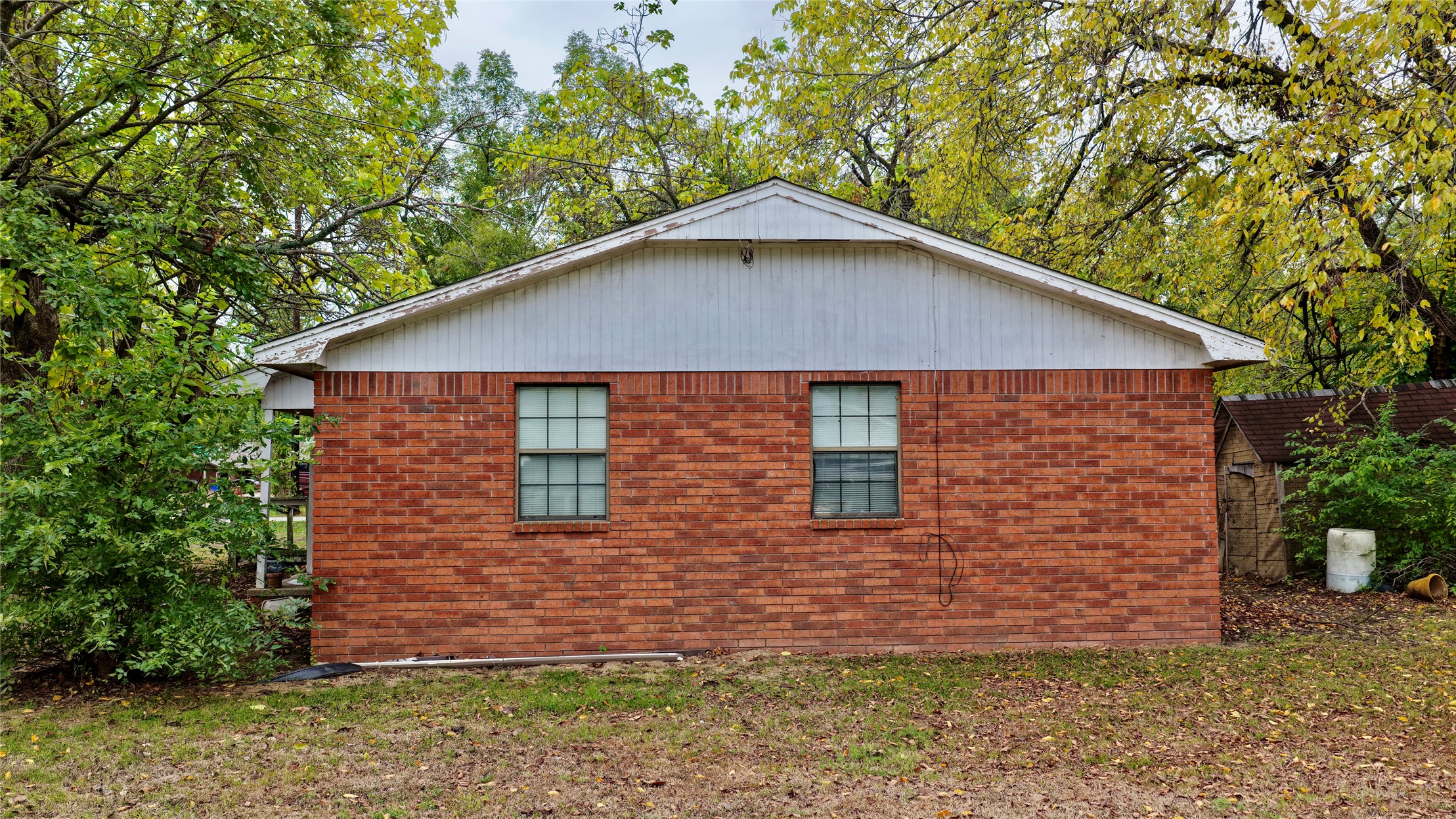 602 Northwest 4th Street Checotah, OK 74426 - Photo 19 of 28 Brick exterior with white gable siding, two windows, and surrounding mature trees