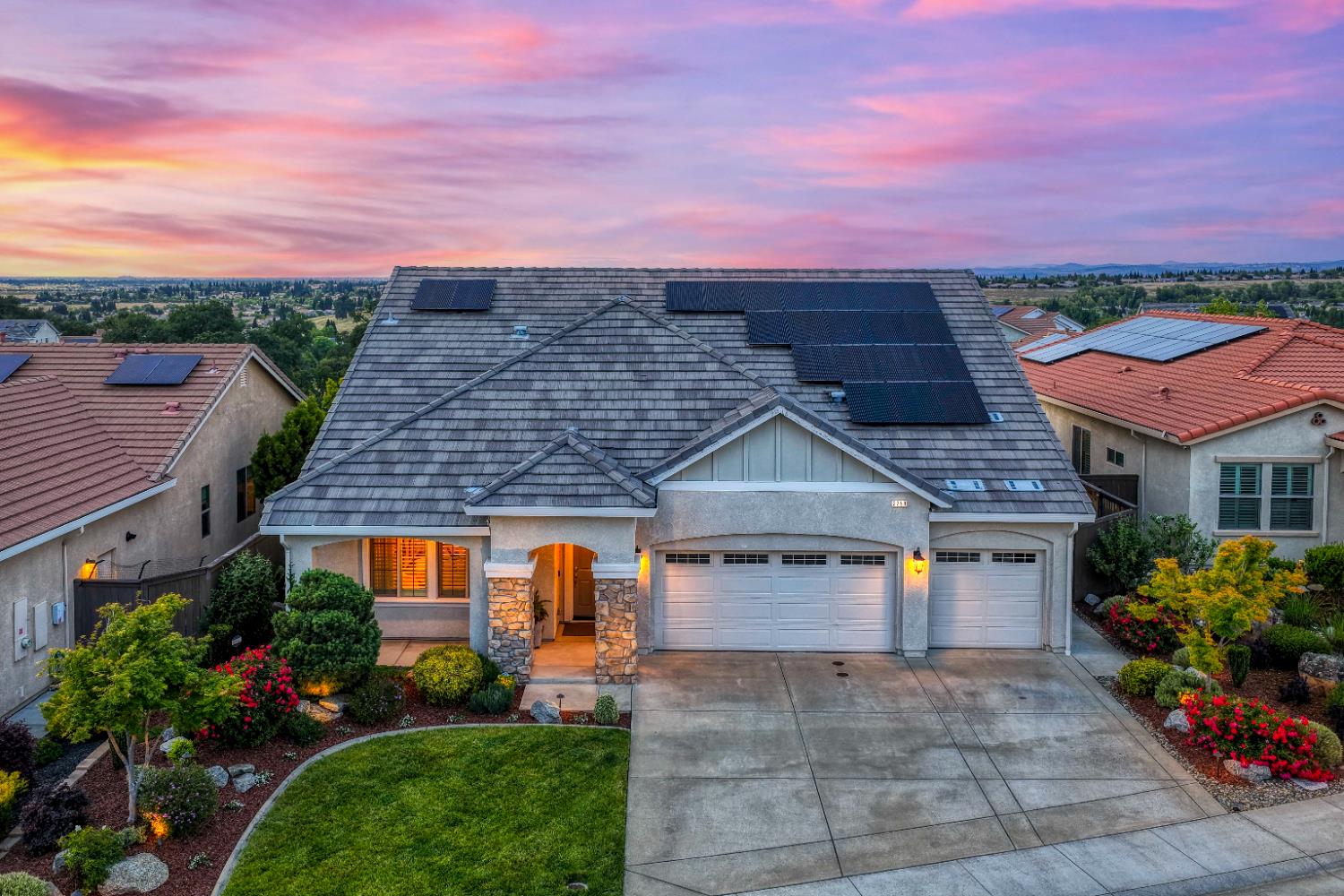 view of front of house with solar panels, driveway, board and batten siding, stone siding, and an attached garage