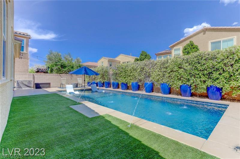 2182 Trivero Street Henderson, NV 89044 - Photo 13 of 14 An inviting swimming pool features water jets alongside a lush lawn and privacy hedges.