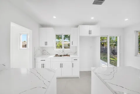 a kitchen with stainless steel appliances kitchen island granite countertop a refrigerator a sink a stove and white cabinets with wooden floor