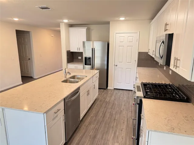 a kitchen with stainless steel appliances a refrigerator a stove a sink and white cabinets