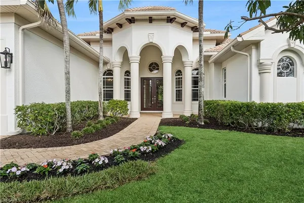 a view of a white house with a large windows and a yard with plants and large tree
