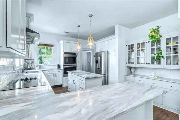 a kitchen with stainless steel appliances granite countertop a refrigerator a oven a sink dishwasher and white cabinets with wooden floor