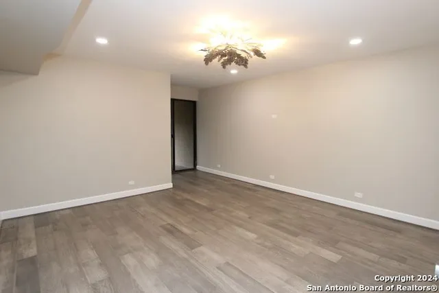 an empty room with a chandelier fan and wooden floor