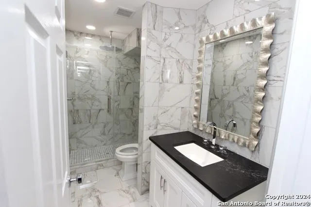 a bathroom with a granite countertop sink a toilet a mirror and shower