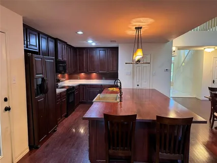 a kitchen with granite countertop a refrigerator a stove a dining table and chairs with wooden floor