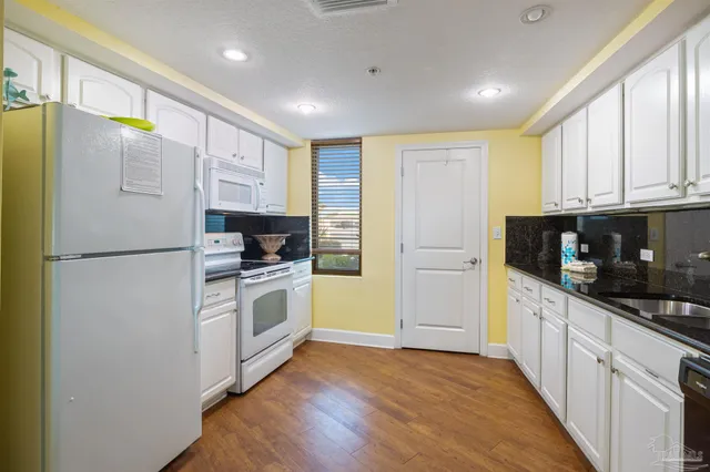 a kitchen with granite countertop a refrigerator a stove a sink and white cabinets with wooden floor