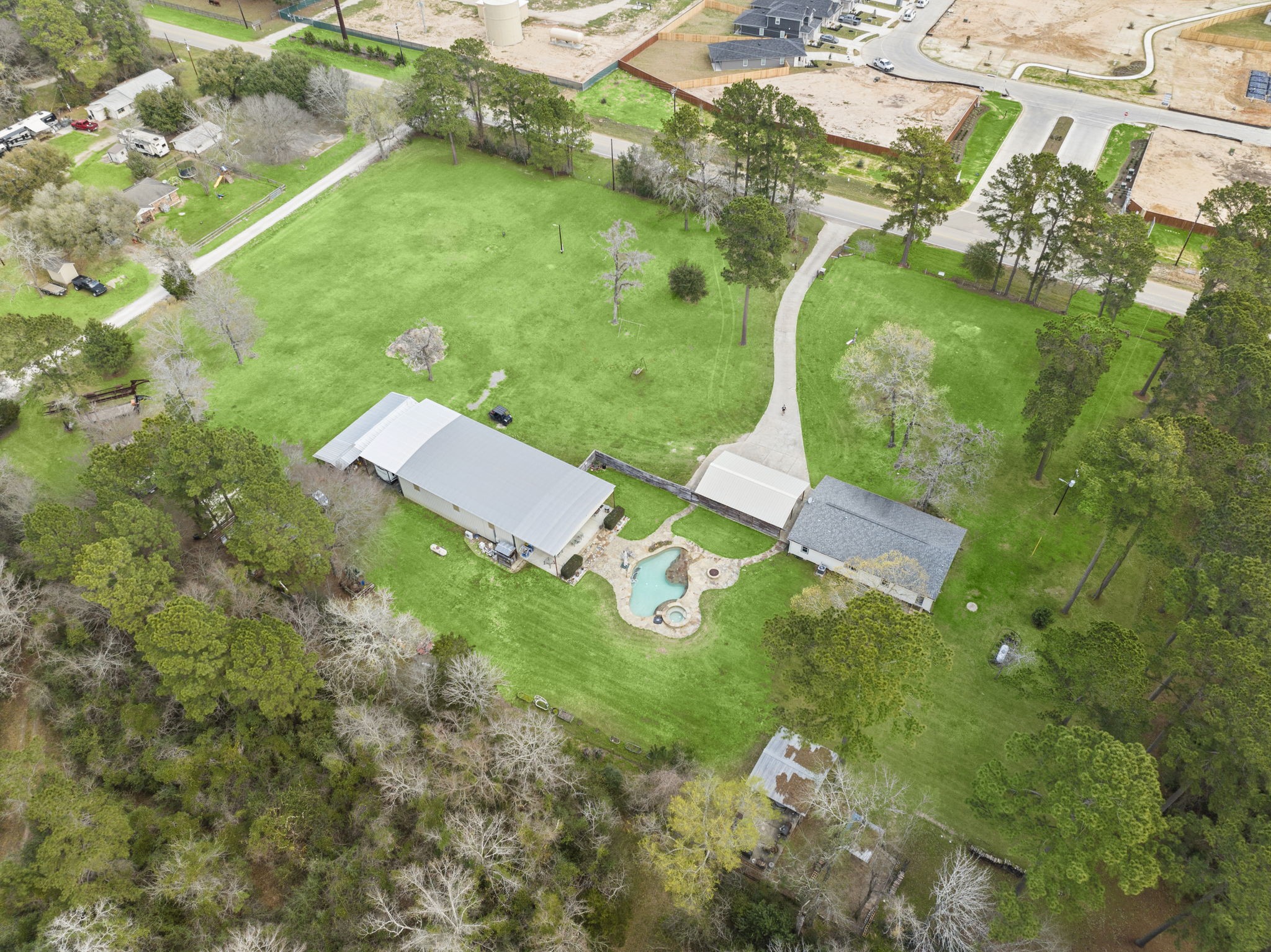 This aerial photo showcases a spacious property featuring a large green lawn, a winding driveway, and a swimming pool. The home has a sizable building with ample surrounding land, ideal for privacy and outdoor activities. The lush trees add to the serene, natural setting.