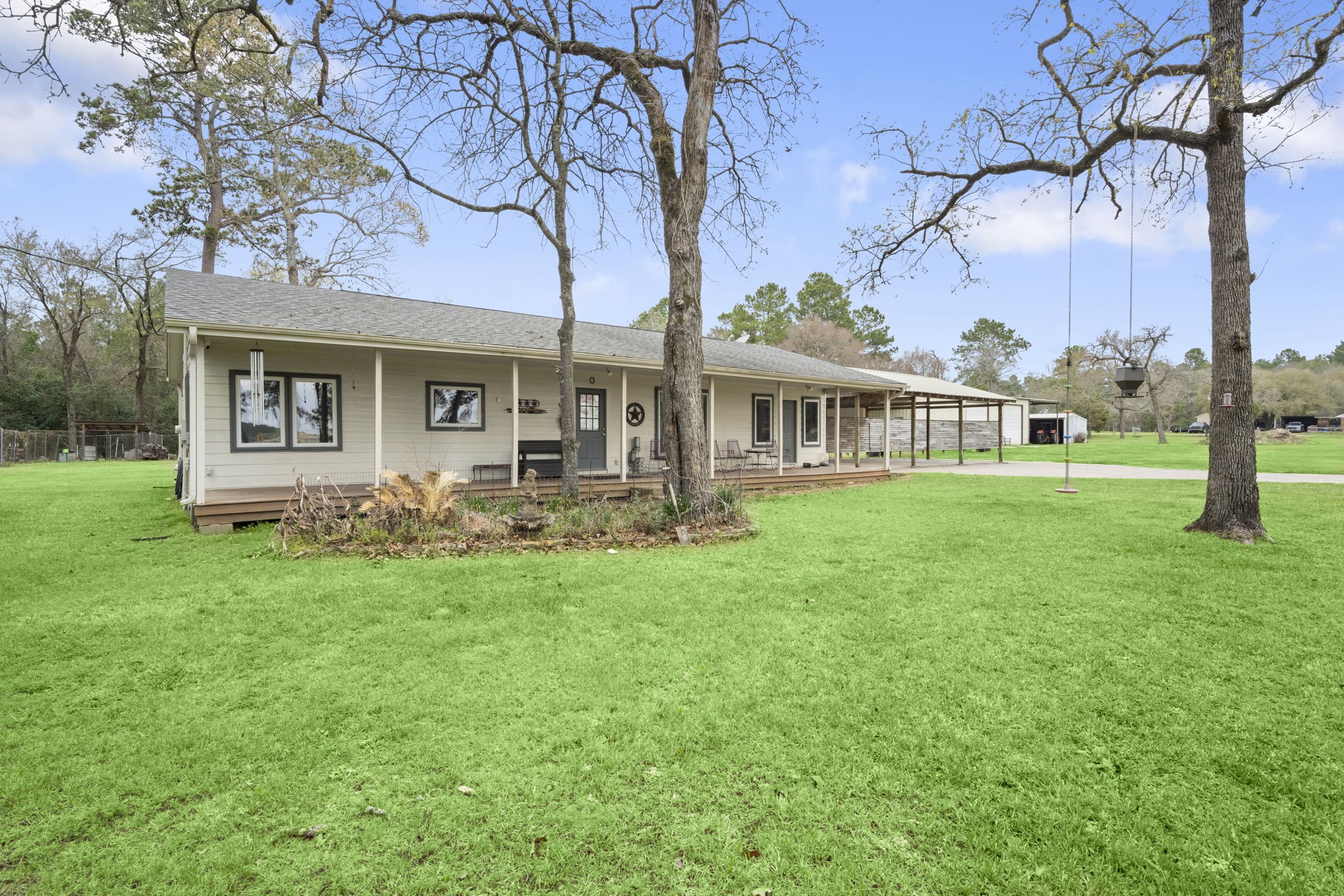 26136 Joseph Road Hockley, TX 77447 - Photo 10 of 31 This photo showcases a charming single-story home with a spacious porch and a large, well-kept lawn. Surrounded by mature trees, it offers a serene, natural setting with ample outdoor space, perfect for relaxation or recreation.