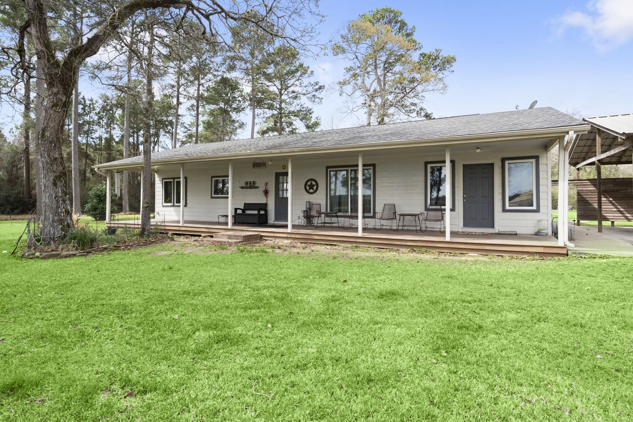 26136 Joseph Road Hockley, TX 77447 - Photo 11 of 31 Charming single-story home with a spacious porch, set amidst a lush, green lawn. Surrounded by mature trees, it offers a tranquil, wooded backdrop. Ideal for those seeking a blend of rustic charm and modern comfort.