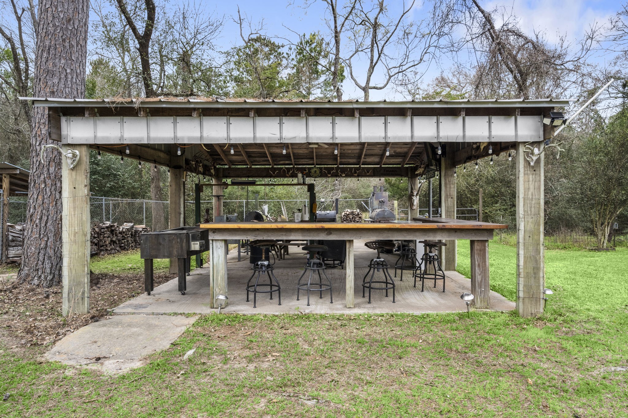 26136 Joseph Road Hockley, TX 77447 - Photo 13 of 31 This photo showcases an inviting outdoor pavilion with a sturdy wooden structure. It features a long bar counter with seating and an open grill area, ideal for entertaining and enjoying the natural surroundings. Stainless countertops!