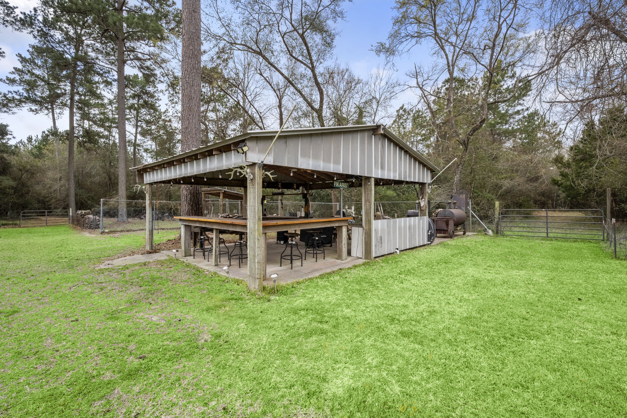 26136 Joseph Road Hockley, TX 77447 - Photo 14 of 31 This photo showcases a charming outdoor pavilion with a bar-style counter and seating, nestled in a spacious, grassy yard surrounded by trees, perfect for entertaining and relaxation.