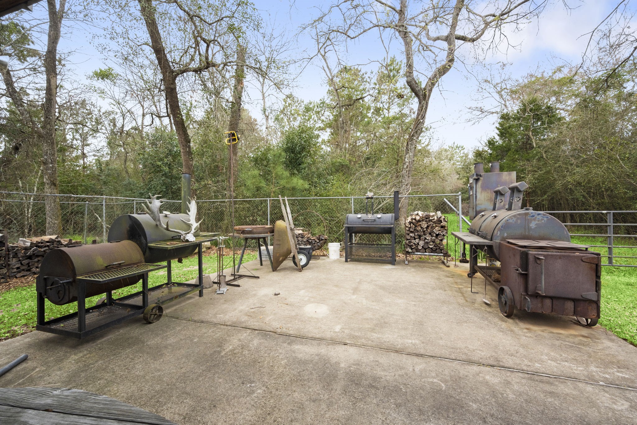 26136 Joseph Road Hockley, TX 77447 - Photo 15 of 31 A spacious backyard patio equipped with multiple grills and smokers, perfect for outdoor cooking and entertaining. The area is surrounded by trees and has a fence for added privacy.