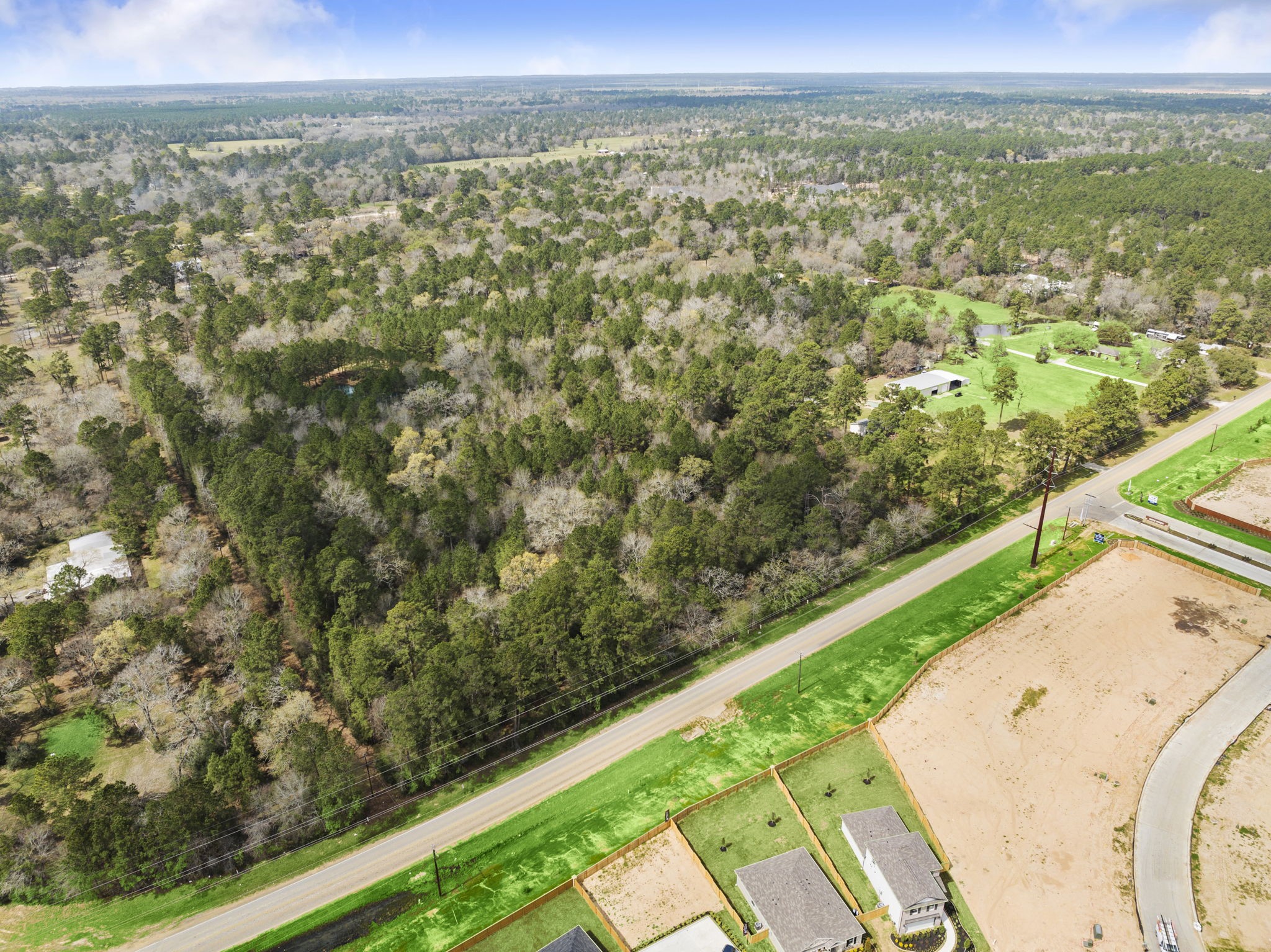 26136 Joseph Road Hockley, TX 77447 - Photo 4 of 31 Expansive aerial view showcasing a densely wooded area alongside a road, with a few homes and open plots nearby, offering a tranquil, rural setting with ample space and privacy.