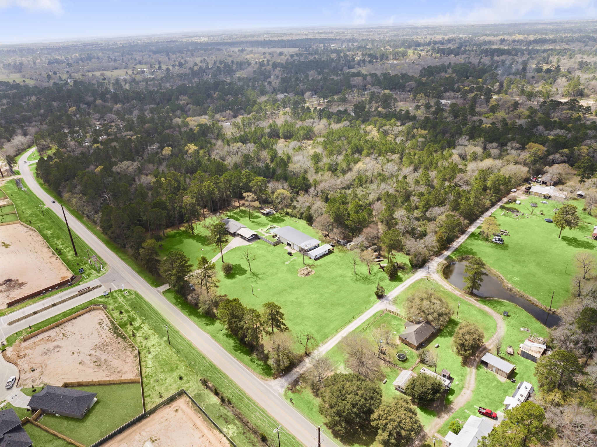 26136 Joseph Road Hockley, TX 77447 - Photo 5 of 31 This aerial photo showcases a spacious rural property surrounded by lush trees, offering a serene and private setting. It features a main house, outbuildings, and a pond, with ample open green space. The property is bordered by a road, providing easy access. Ideal for those seeking tranquility and nature.