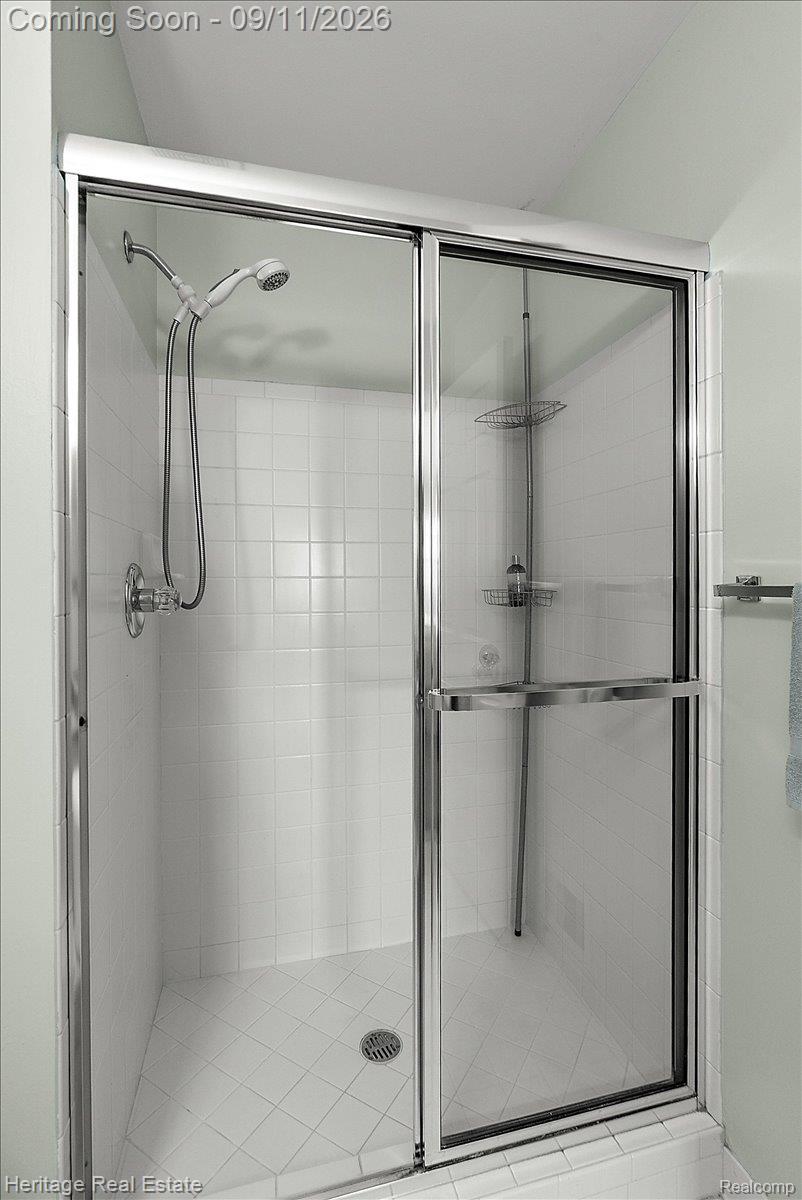 3088 High Pointe Ridge Road Lake Orion, MI 48359 - Photo 16 of 31 Sliding glass shower enclosure with chrome hardware, white tile surround, and an adjustable showerhead