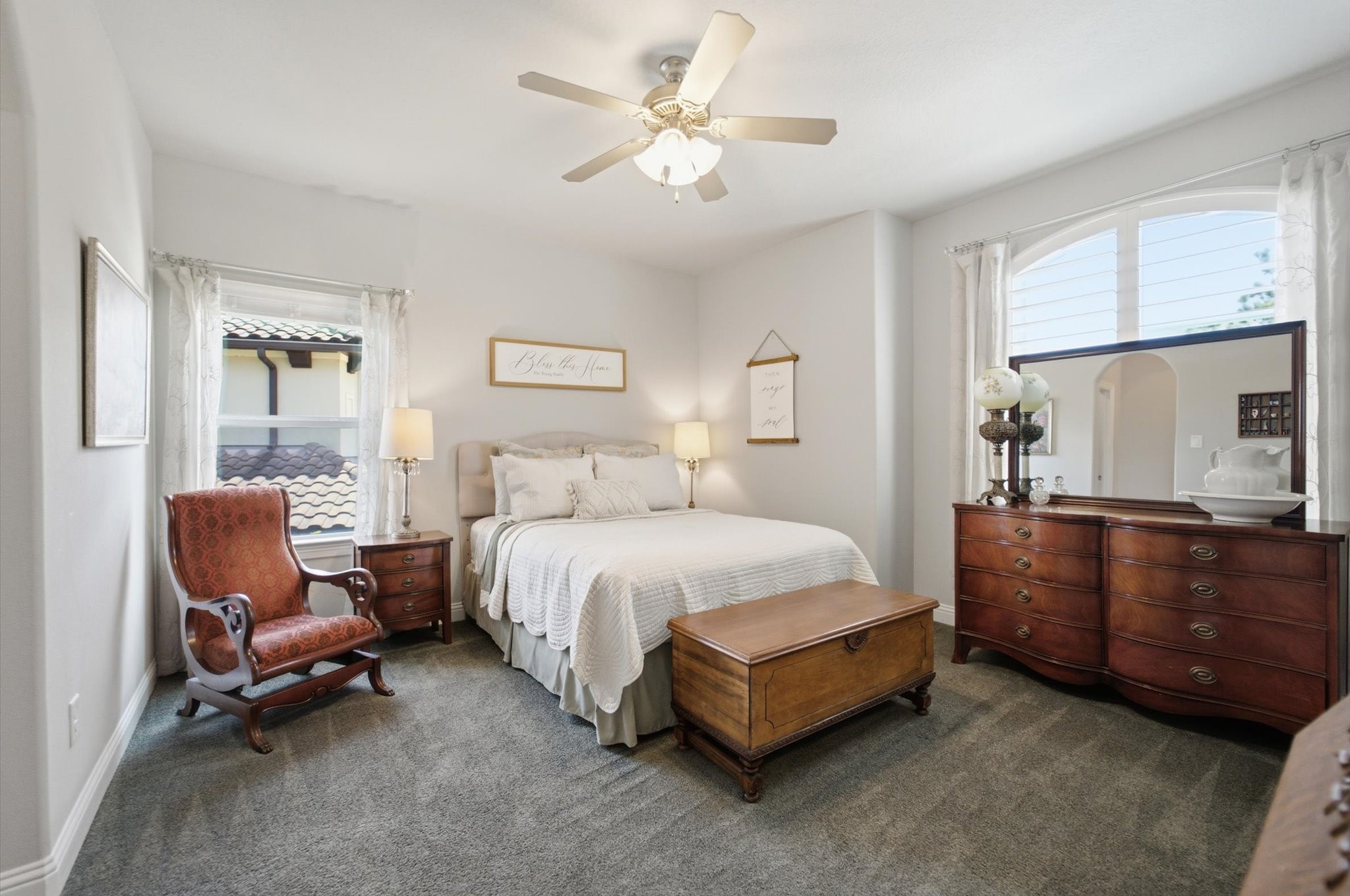 23722 Thortons Park Lane Spring, TX 77389 - Photo 36 of 48 This cozy bedroom features a comfortable bed with elegant bedding, flanked by bedside tables and lamps. It has a large window allowing natural light, a ceiling fan, a classic dresser with a mirror, and an armchair, creating a warm and inviting atmosphere.