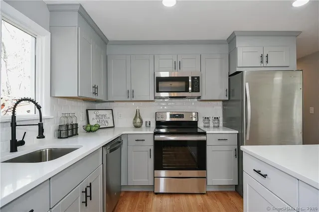 a kitchen with stainless steel appliances white cabinets a sink a stove a refrigerator and microwave