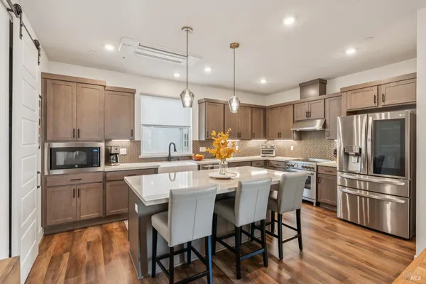 a kitchen with stainless steel appliances kitchen island granite countertop a dining table chairs sink and cabinets