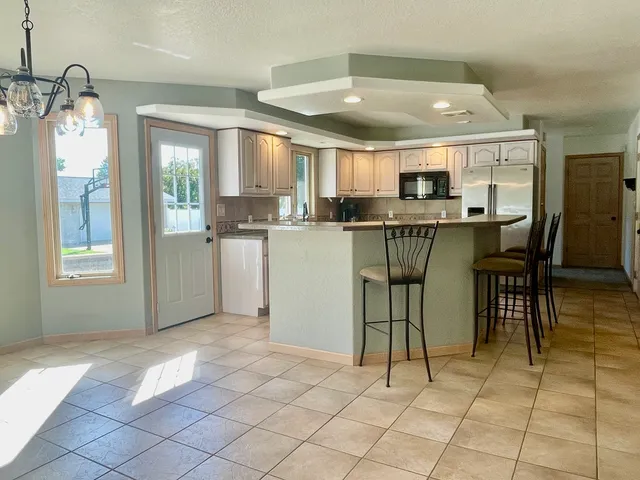 a kitchen with stainless steel appliances kitchen island granite countertop a refrigerator a stove a dining table and chairs with wooden floor