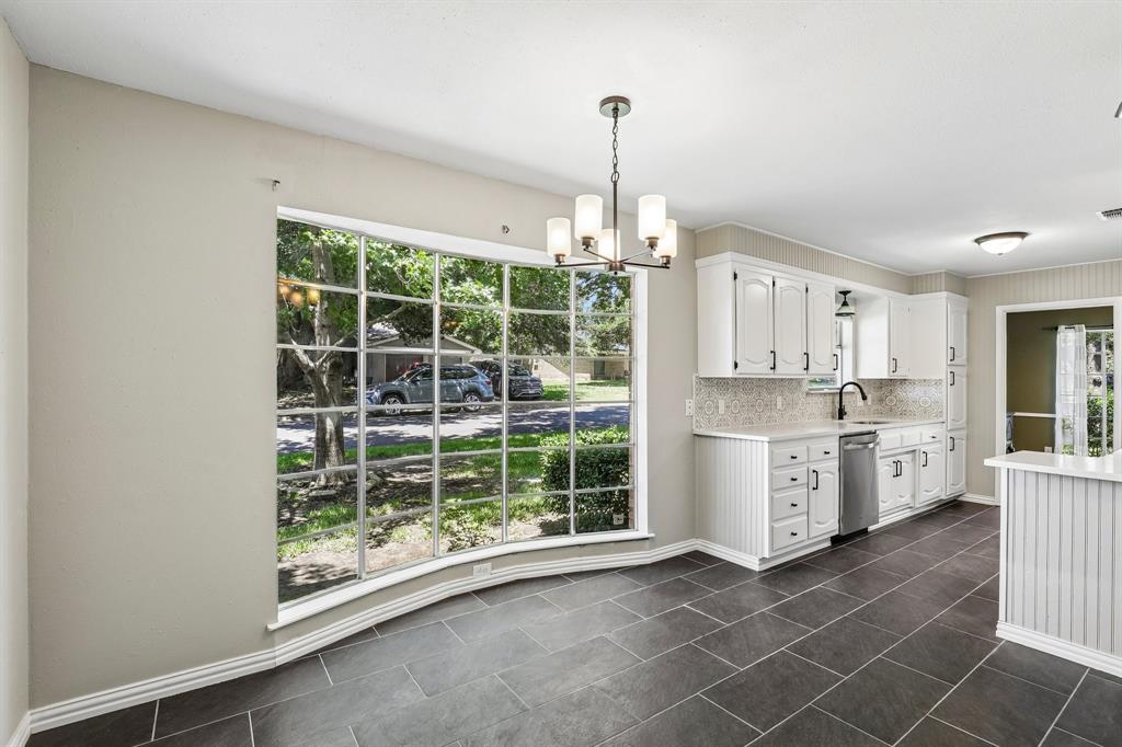 1600 South Timber Court Benbrook, TX 76126 - Photo 9 of 30 Spacious interior featuring a large bay window, dark tile flooring, white cabinetry with dark hardware, a stainless steel dishwasher, and a bronze chandelier
