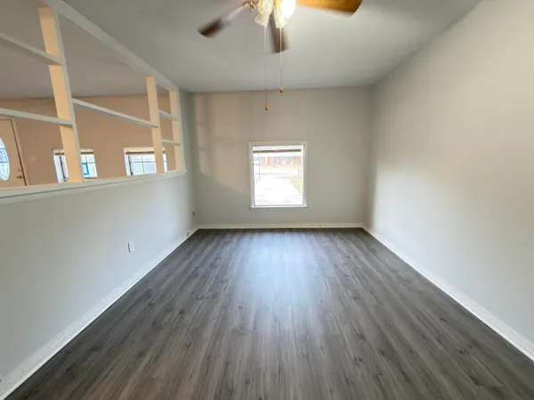 an empty room with wooden floor chandelier fan and windows