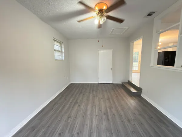 an empty room with wooden floor chandelier fan and windows