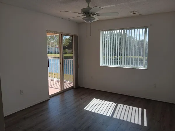 an empty room with wooden floor fan and windows