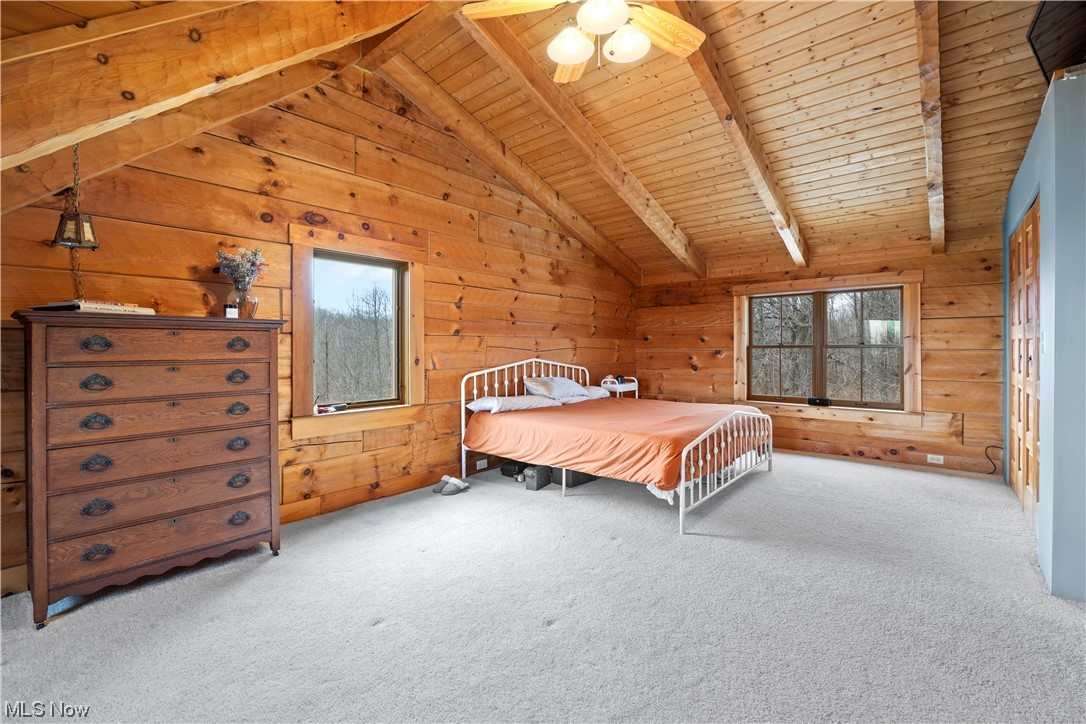 9485 Stone Road Litchfield, OH 44253 - Photo 31 of 50 Carpeted bedroom with beamed ceiling, ceiling fan, high vaulted ceiling, wooden ceiling, and wood walls