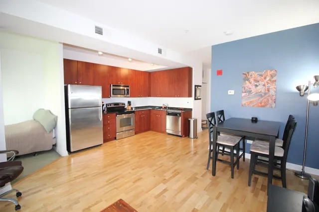 a kitchen with stainless steel appliances granite countertop a refrigerator a stove a sink a dining table and chairs with wooden floor