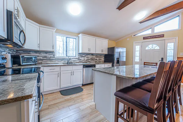 a kitchen with stainless steel appliances granite countertop a stove a sink dishwasher a microwave oven and a dining table with wooden floor