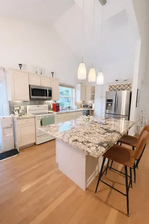 a kitchen with kitchen island granite countertop a stove top oven a sink dishwasher and white cabinets with wooden floor