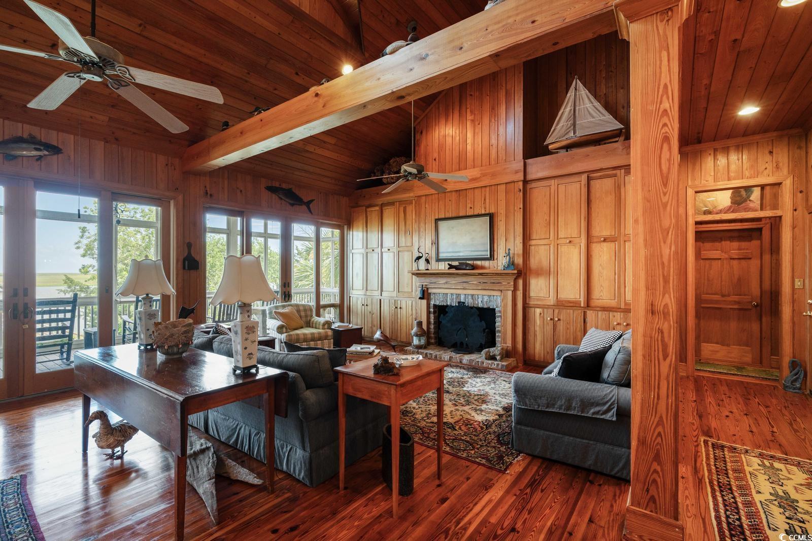 315 Lofton Court McClellanville, SC 29458 - Photo 25 of 40 Living room featuring a ceiling fan, wooden walls, a fireplace with raised hearth, a wooden ceiling with exposed beams, and hardwood / wood-style flooring