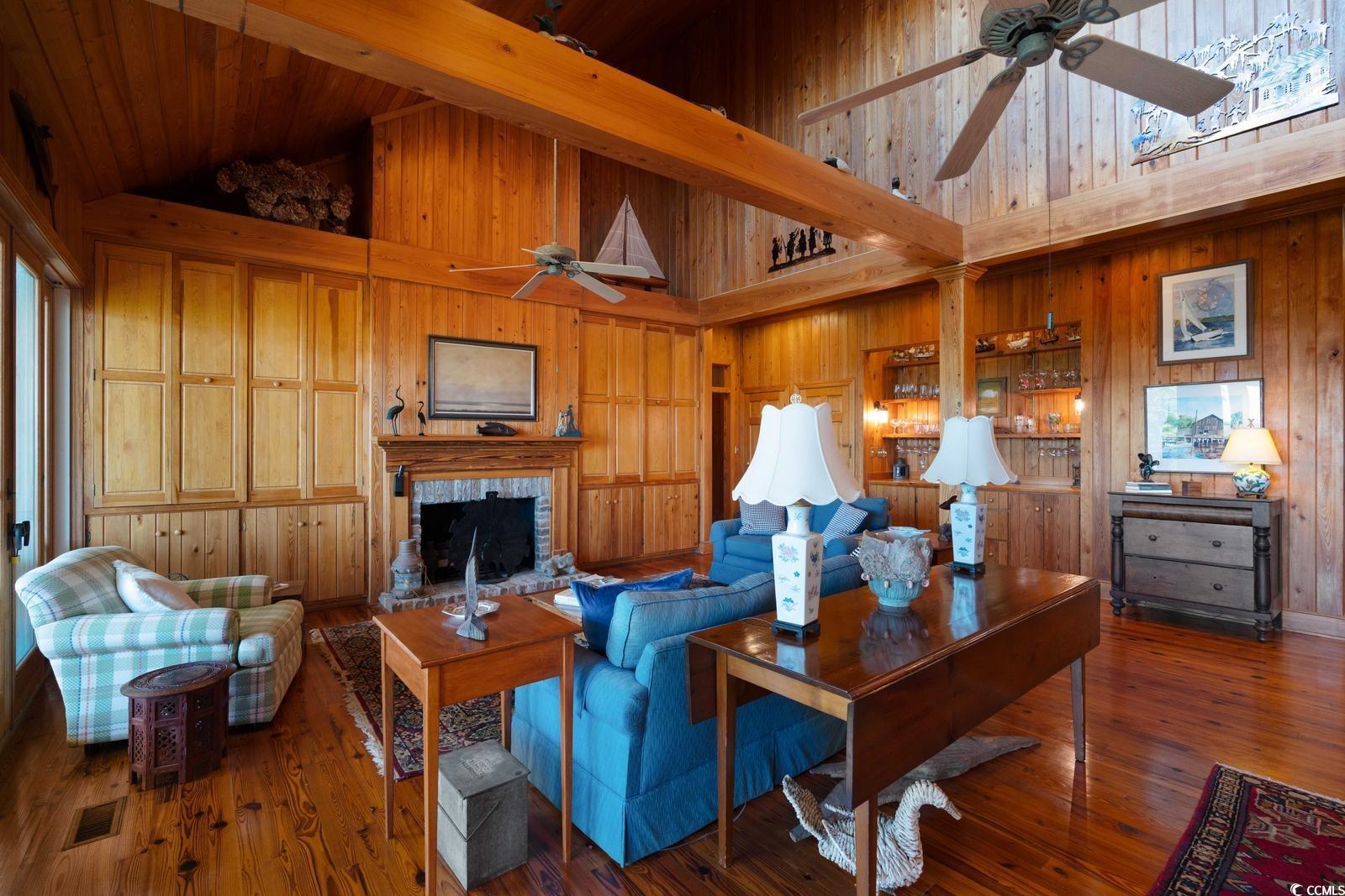 315 Lofton Court McClellanville, SC 29458 - Photo 26 of 40 Living room with a ceiling fan, high vaulted ceiling, wood walls, a fireplace with raised hearth, and wood-type flooring