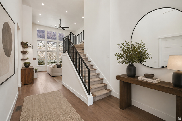 692 East Mountain Road North Ogden, UT 84414 - Photo 10 of 35 Two-story entryway featuring wood-finish flooring, a carpeted staircase with black metal railings, and a multi-pane window wall